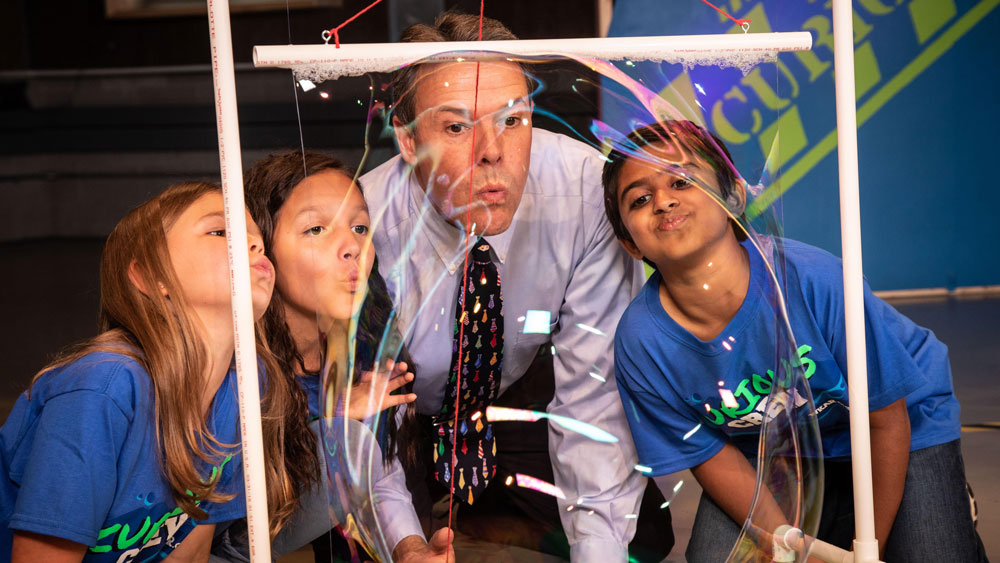 Curious Crew - Image of host with students doing an experiment.