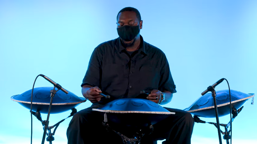 A Black man in a face mask plays a set of 3 steel drums