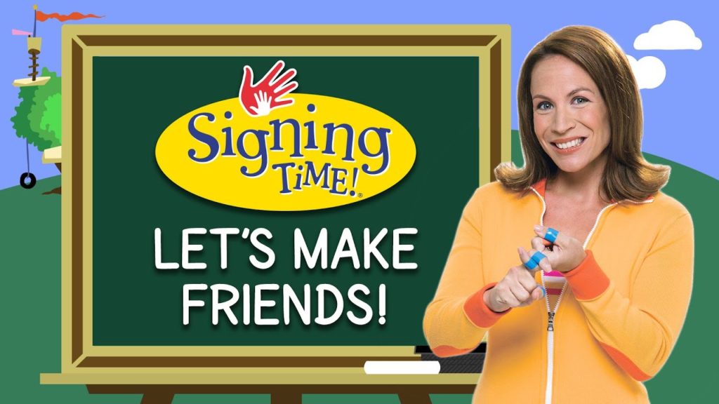 A white woman with brown hair smilingat the camerawith a graphic of a chalkboard beside her. The Signing Time logo is over the chalkboard.