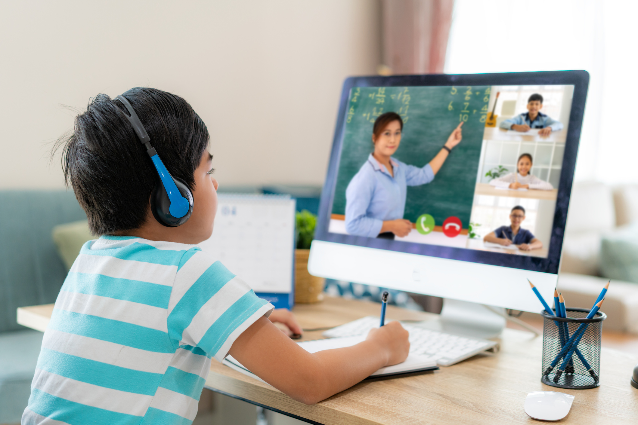 Asian boy student video conference e-learning with teacher and classmates on computer in living room at home.