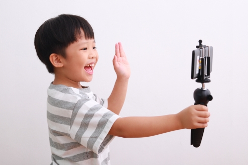 Cheerful little boy using smartphone and mini tripod filming video, vlogging