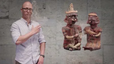 A man gestures to a superimposed image of two statues