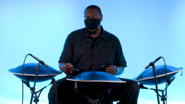 A Black man in a face mask plays a set of 3 steel drums